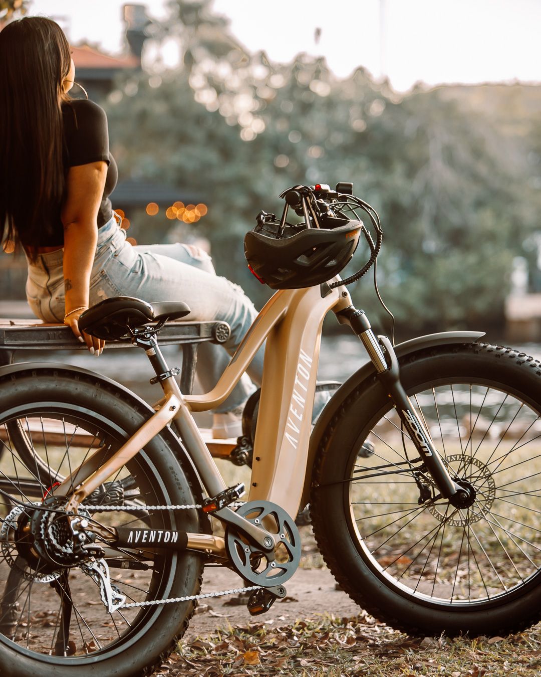 Electric bike parked on trail at sunset with person sitting nearby in soft lighting.