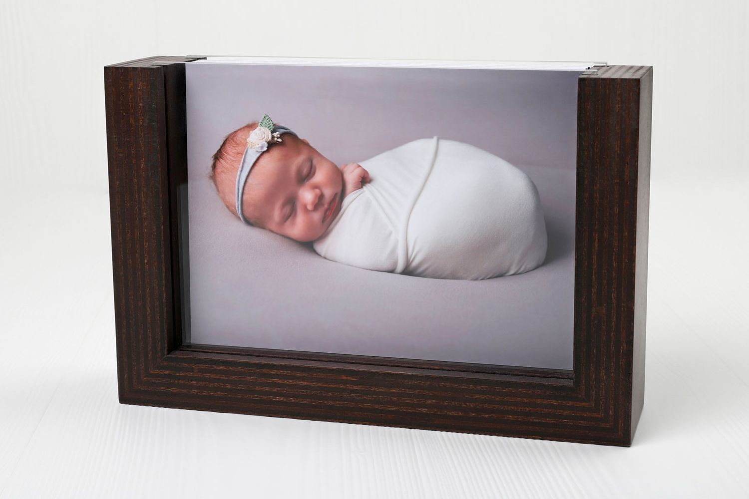 Un portrait de nouveau-né encadré dans un support en bois sombre, montrant un bébé emmailloté.