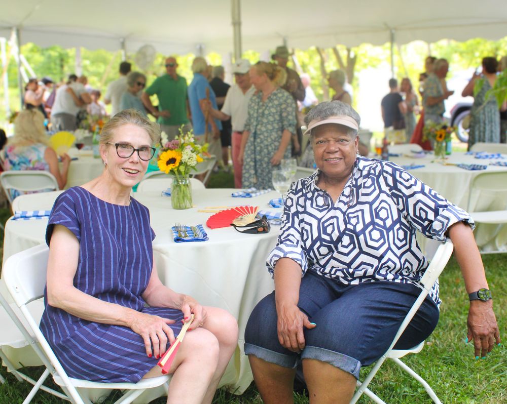 Two guests enjoying conversation at an outdoor event with table settings visible in background.
