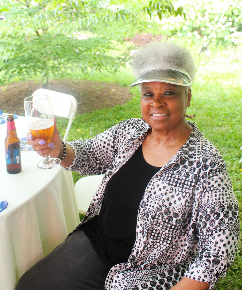 Woman in patterned jacket smiles while enjoying beverage at outdoor event.