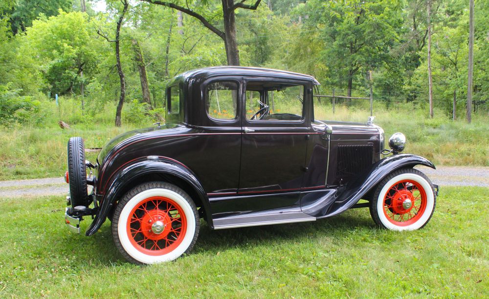 Classic black 1930s Ford Model A coupe with red wheels displayed on grass.