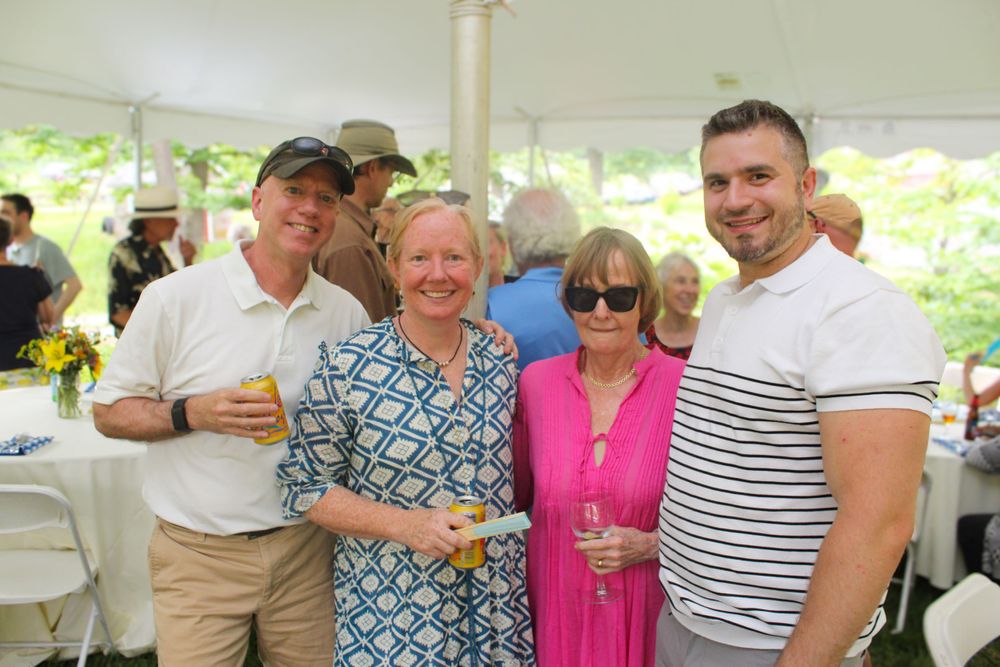 A group socializing with drinks under a white tent at an outdoor summer party.
