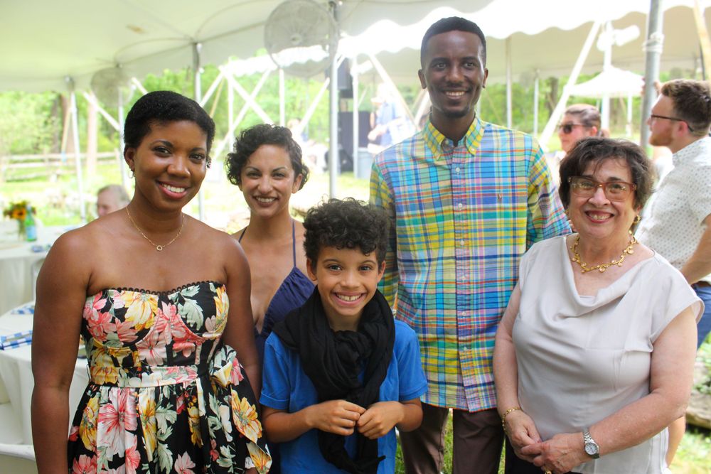A cheerful group of people gathered for a photo at an outdoor party under a tent.