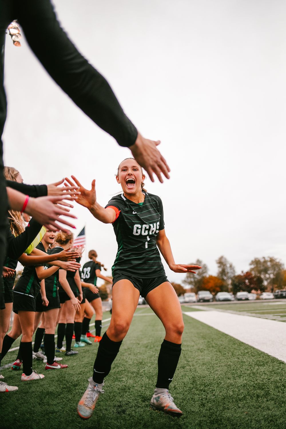 Excited female soccer player in black GCHS jersey high-fiving teammates during pre-game lineup.