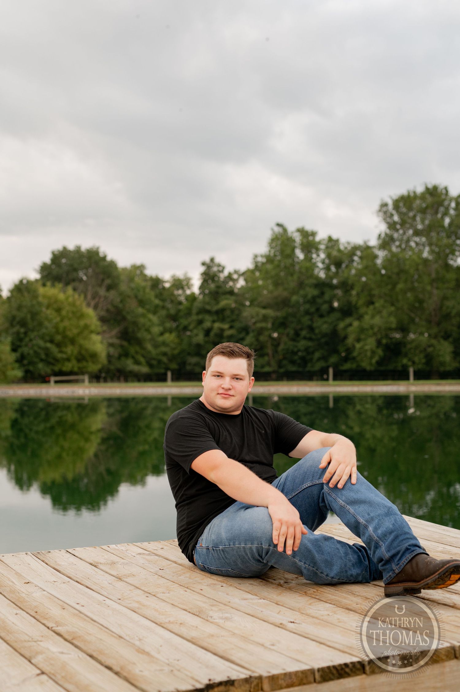A person relaxes on wooden dock by serene lake under cloudy skies.