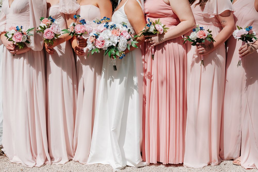 Close-up view of floral bouquets held against pink and white bridesmaid dresses at a wedding.