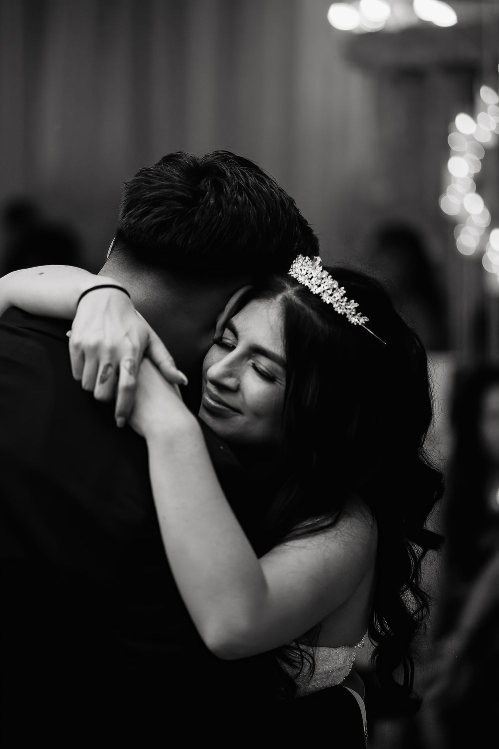 Romantic black and white photo of a bride in a tiara embracing her partner during their wedding dance.