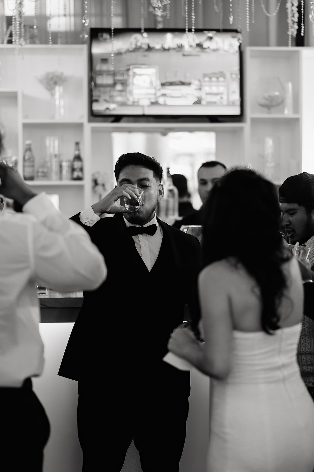 A black and white photo showing a wedding celebration at a bar with guests in formal attire.