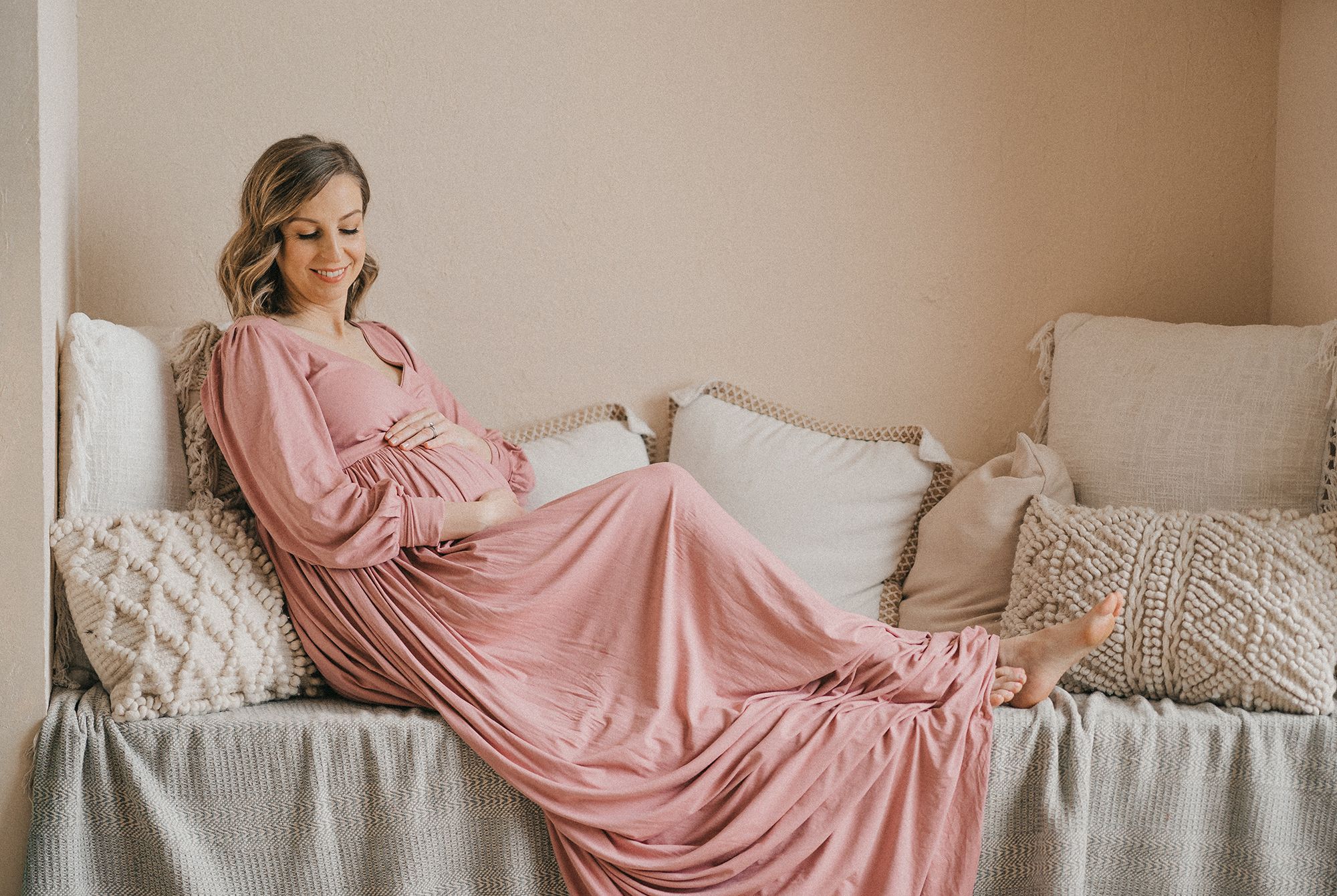 pregnant woman is on the couch with the pillows in Lounge room at Mint Room studio posing for a maternity photo session