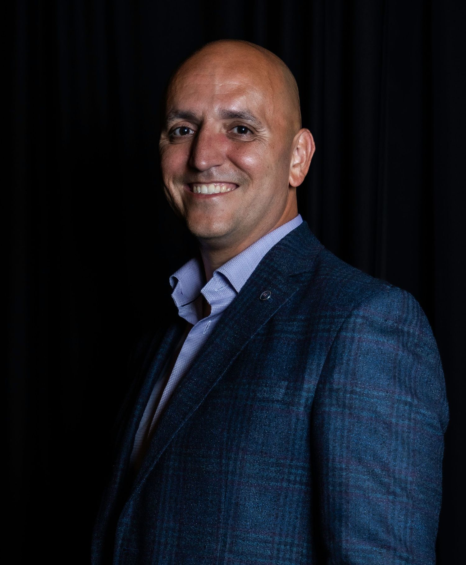 Corporate headshot series featuring someone in a blue plaid suit against black background. Woman owned, headshot