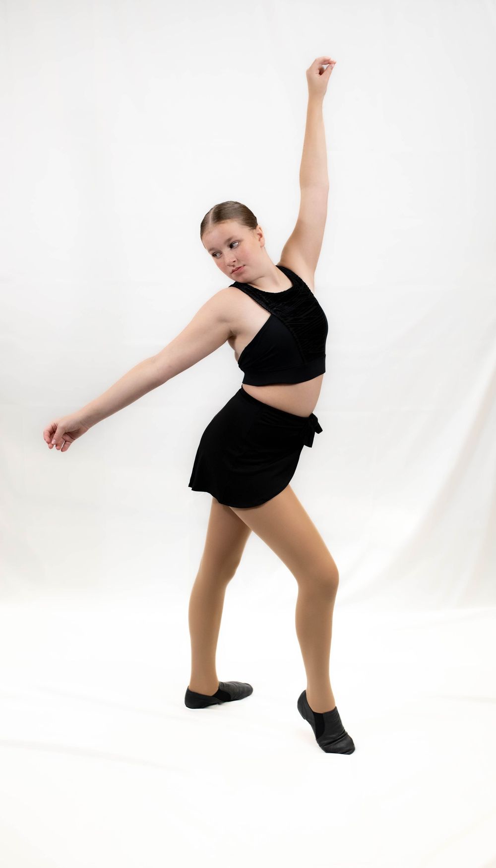 A dancer in black athletic wear performs a dynamic pose with one arm raised and legs in motion against a white backdrop.