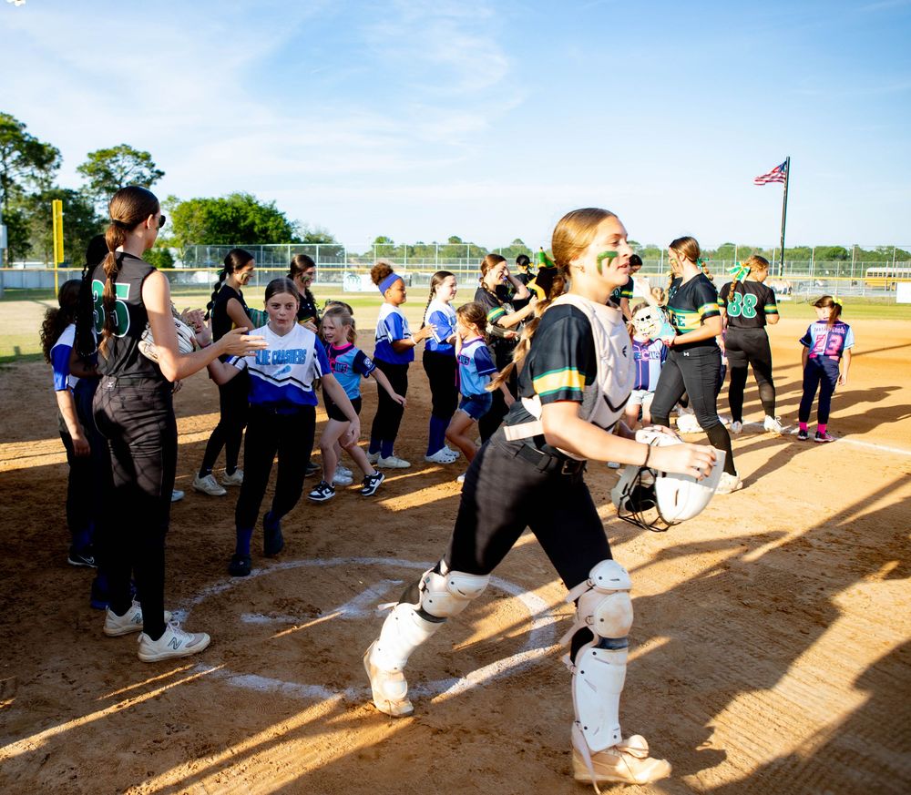 A series of people line up to participate in a team building exercise at an outdoor baseball field during daytime.
