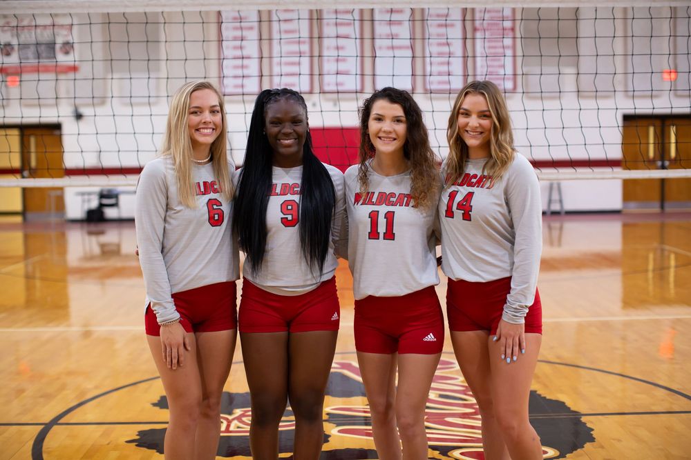 High school volleyball players pose together in their red and white team uniforms in a gymnasium.