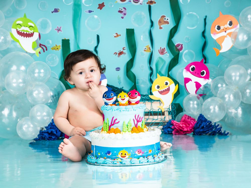 Baby's first birthday cake smash with Baby Shark theme, featuring decorated cake, balloons, and colorful ocean backdrop.