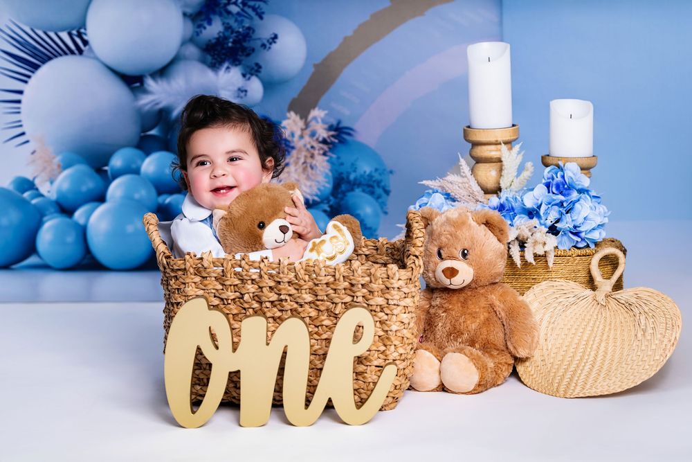First birthday photo setup with teddy bears, piano, and blue balloon decorations.