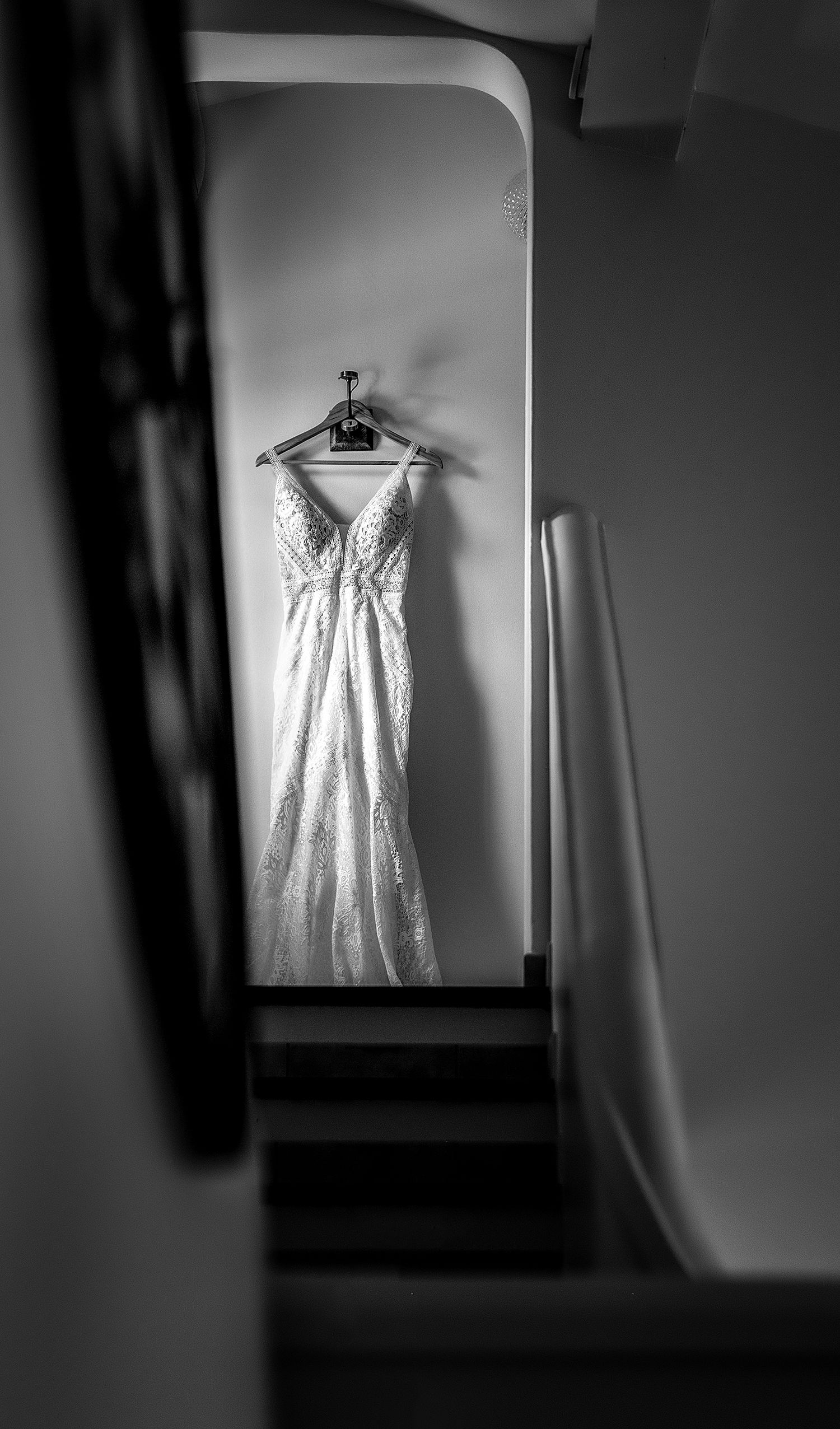 White wedding dress hanging elegantly in dramatic black and white stairwell lighting.