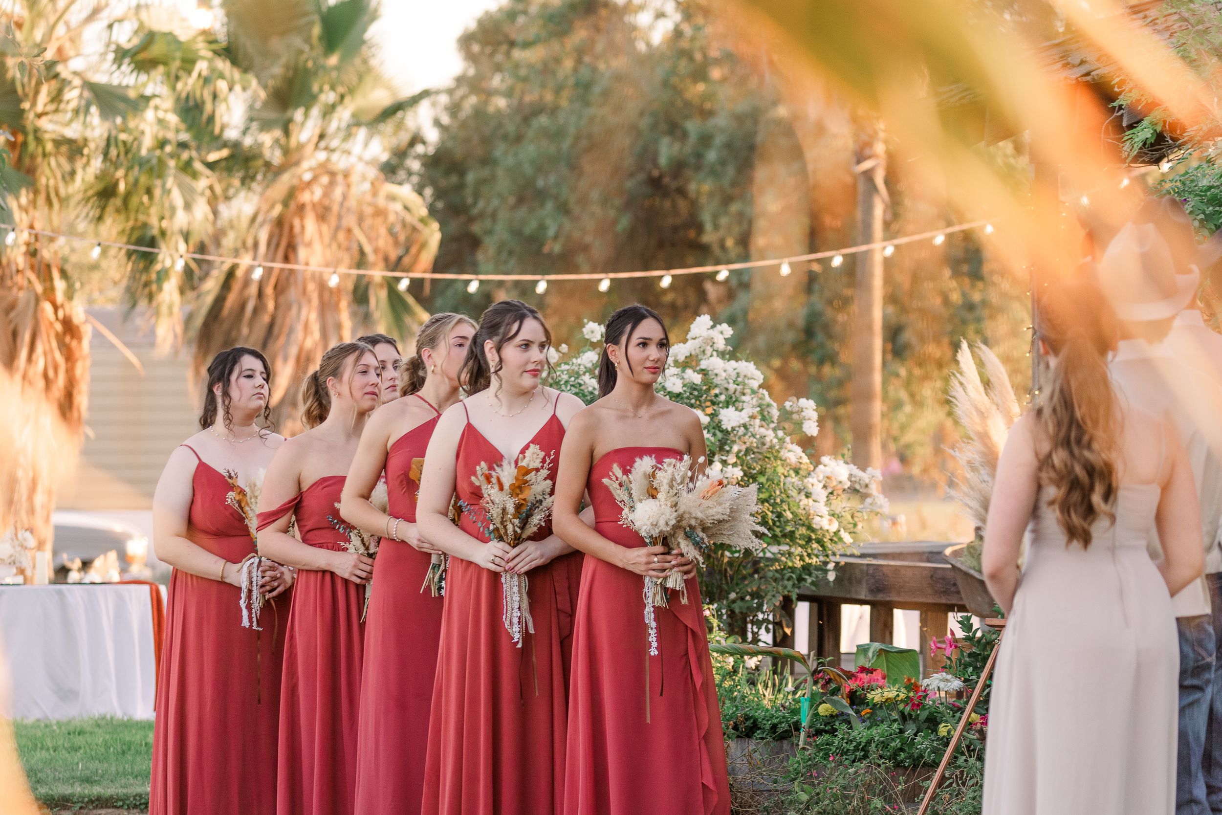 Wedding party in coral dresses posing outdoors during golden hour.