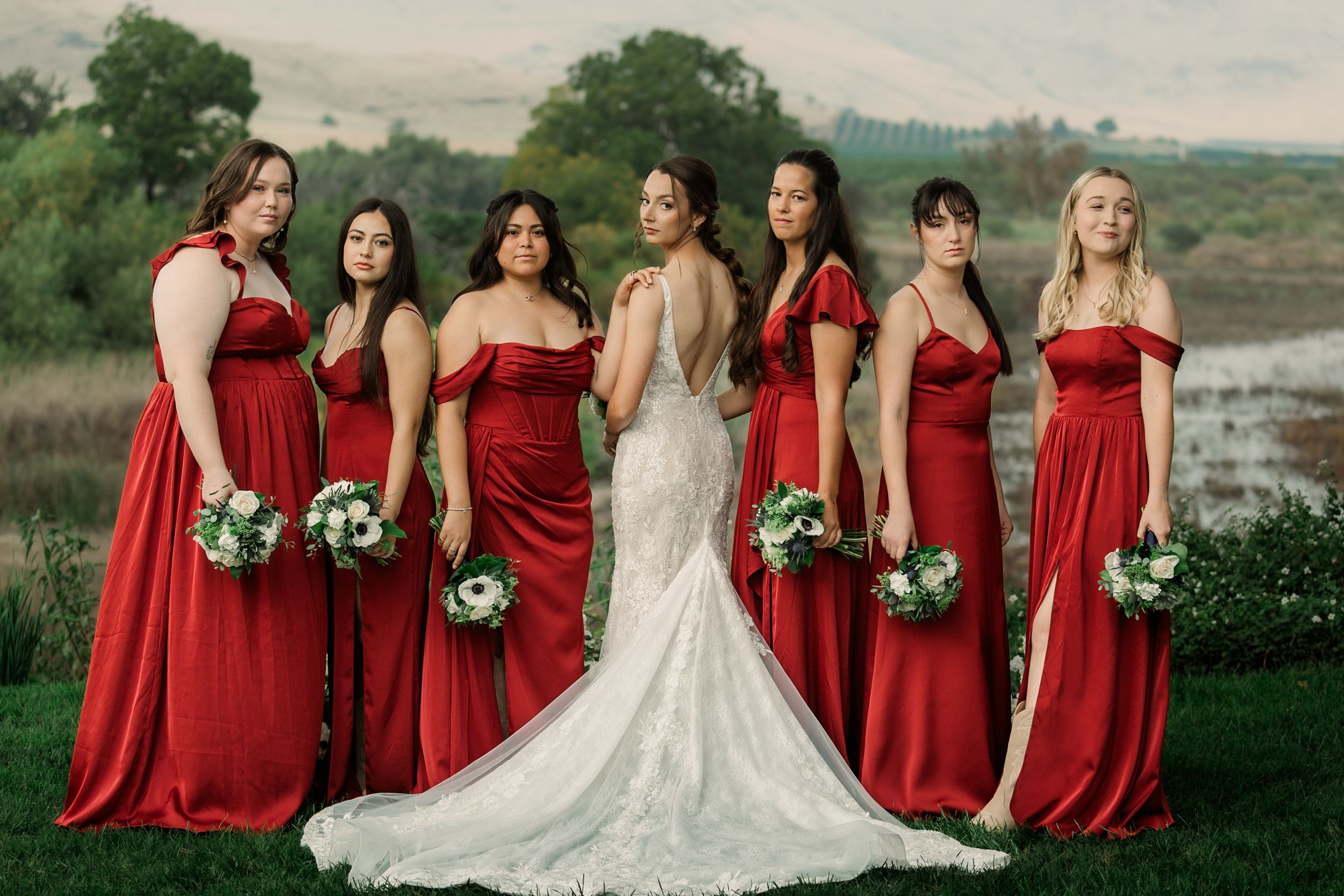 Bridal party in red dresses poses together on a scenic hillside.