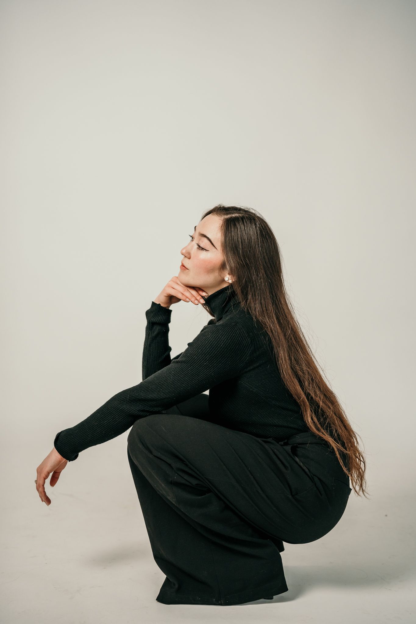 A person in black clothing strikes dramatic poses against a white background in a four-image artistic series.