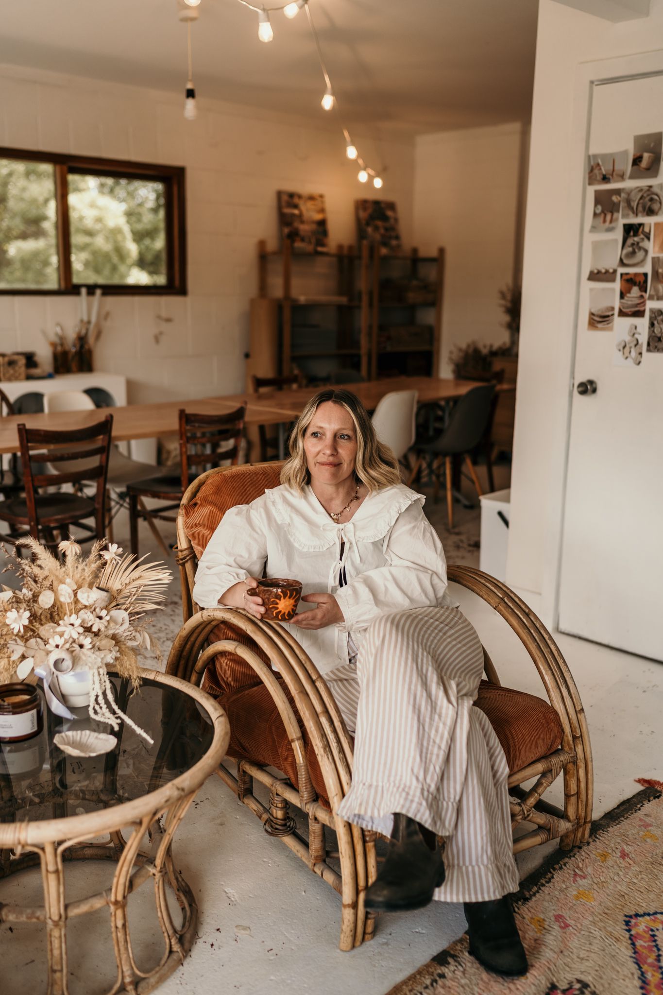 Interior view of someone relaxing in a rattan chair wearing a flowing white dress in Christchurch pottery studio.