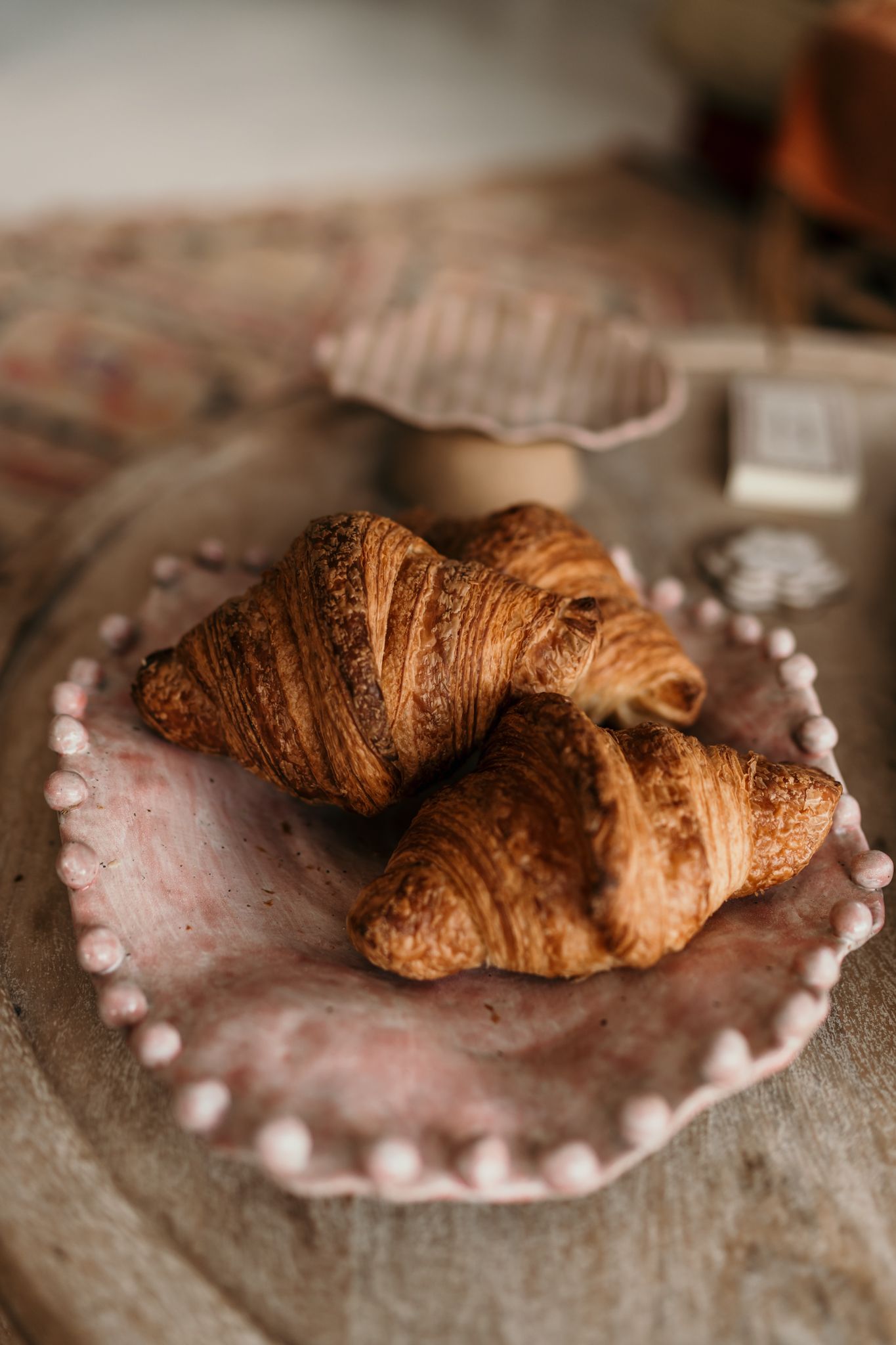 Two golden brown croissants displayed on a scalloped pink ceramic plate in Christchurch pottery studio.