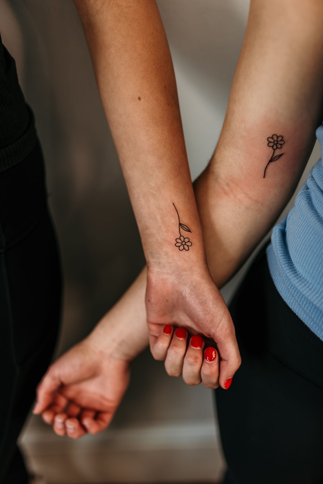 Two arms displaying matching small flower tattoos in minimalist style in in Christchurch tattoo studio.