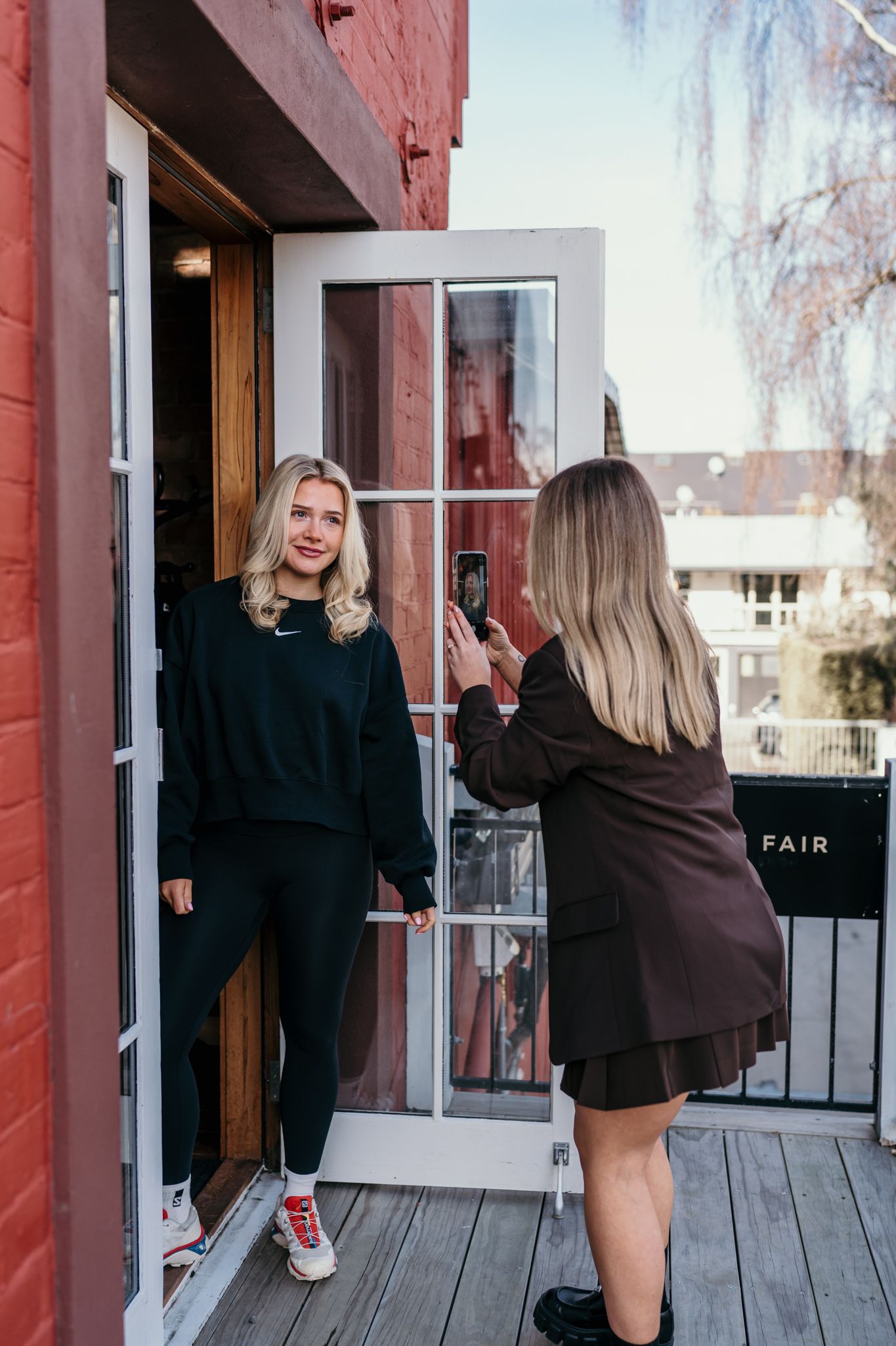 A photographer captures content on a porch with red brick walls and a white screen door in a casual outdoor setting.