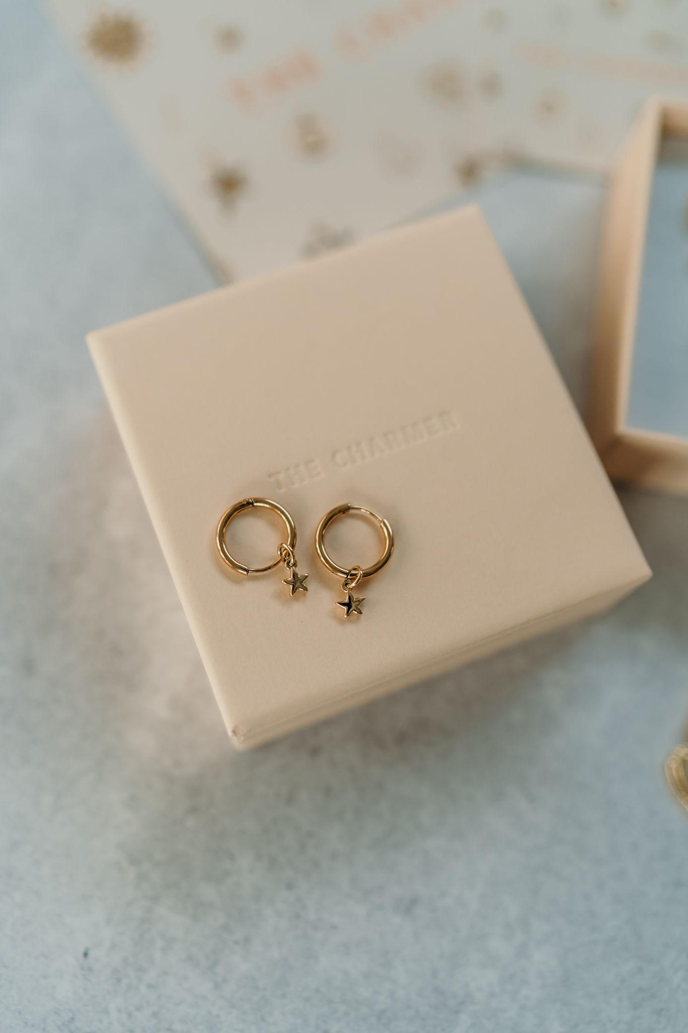 Close-up view of delicate gold star hoop earrings displayed on a beige stone ring holder.