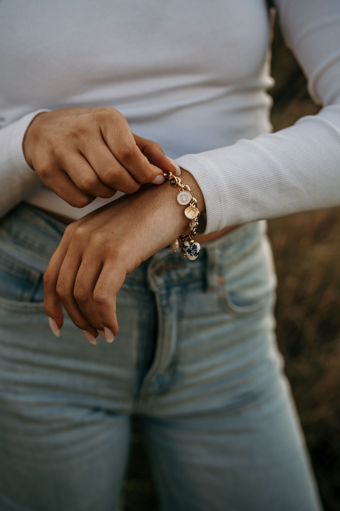 Close-up shot of hands adjusting a silver charm bracelet while wearing light blue jeans and white sweater.