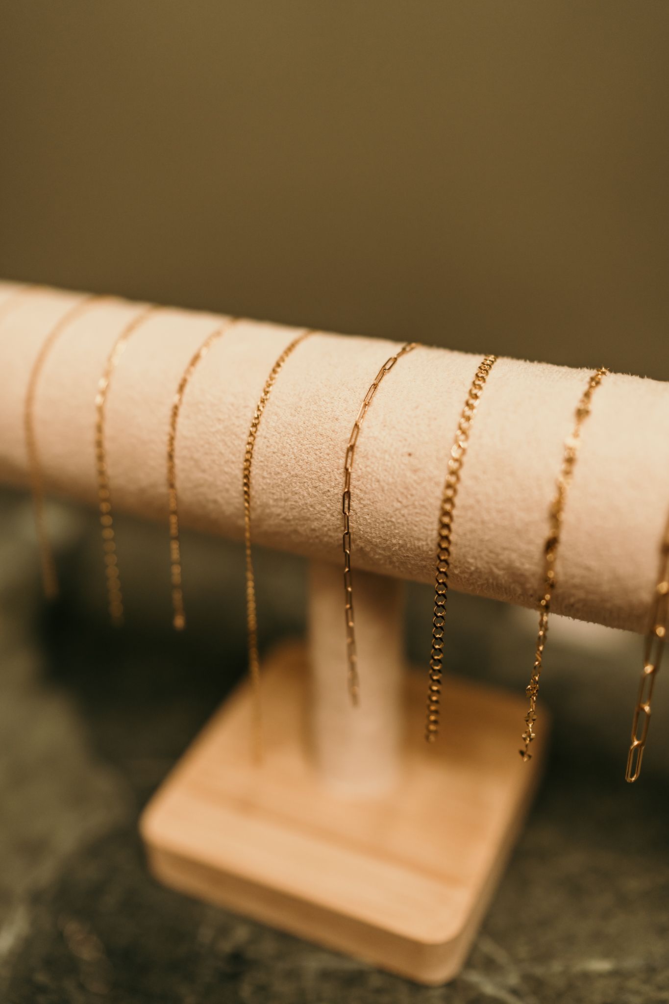 Delicate gold chains displayed on a beige velvet jewelry stand against a dark background.