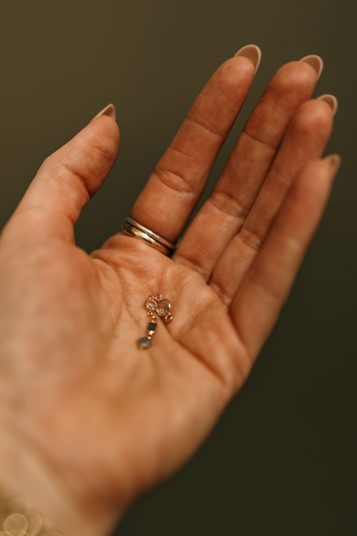 An open palm with a gold wedding band displays a small key-shaped pendant against a dark background.