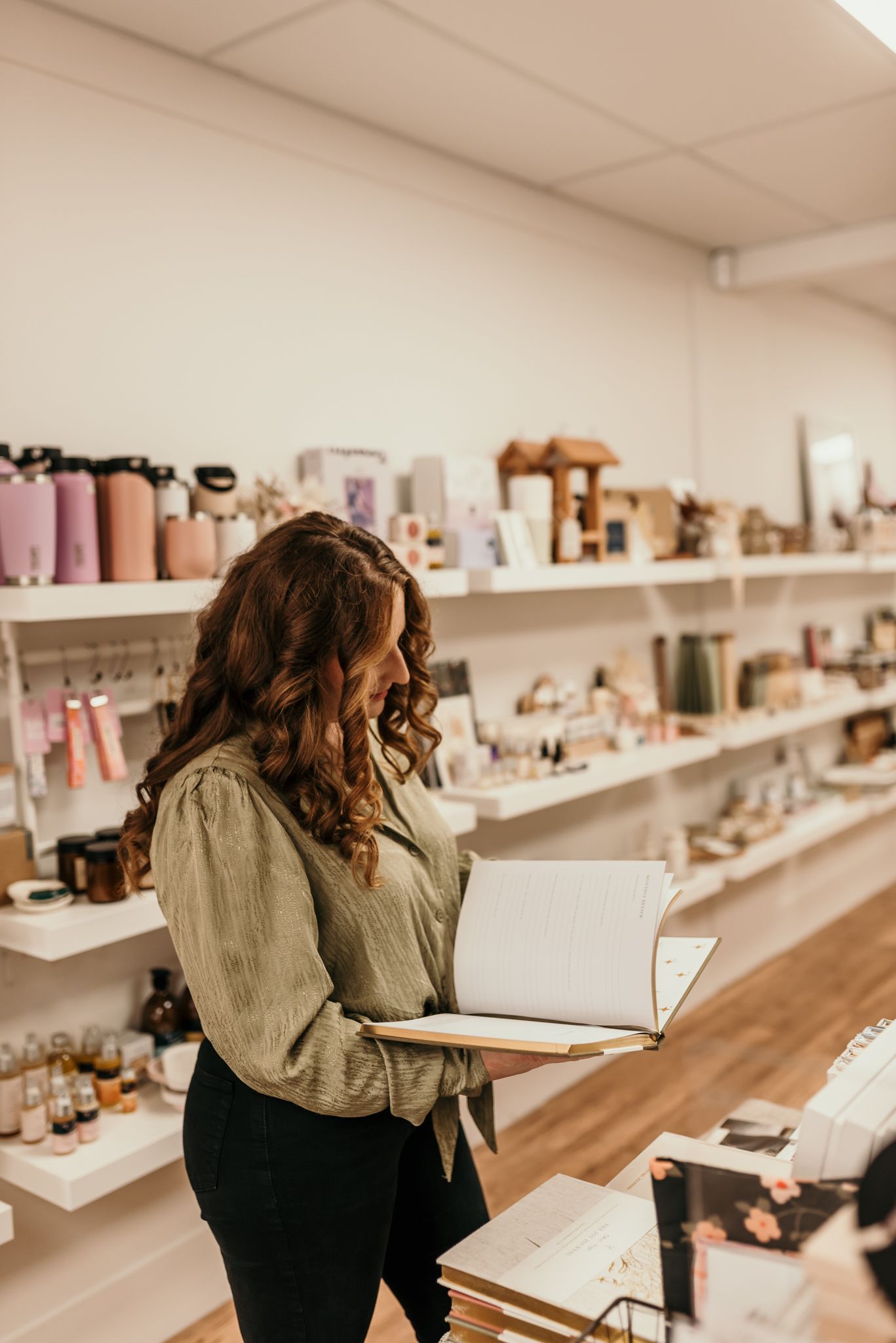 Person in olive green sweater browsing items in a retail shop with white shelving in Christchurch.
