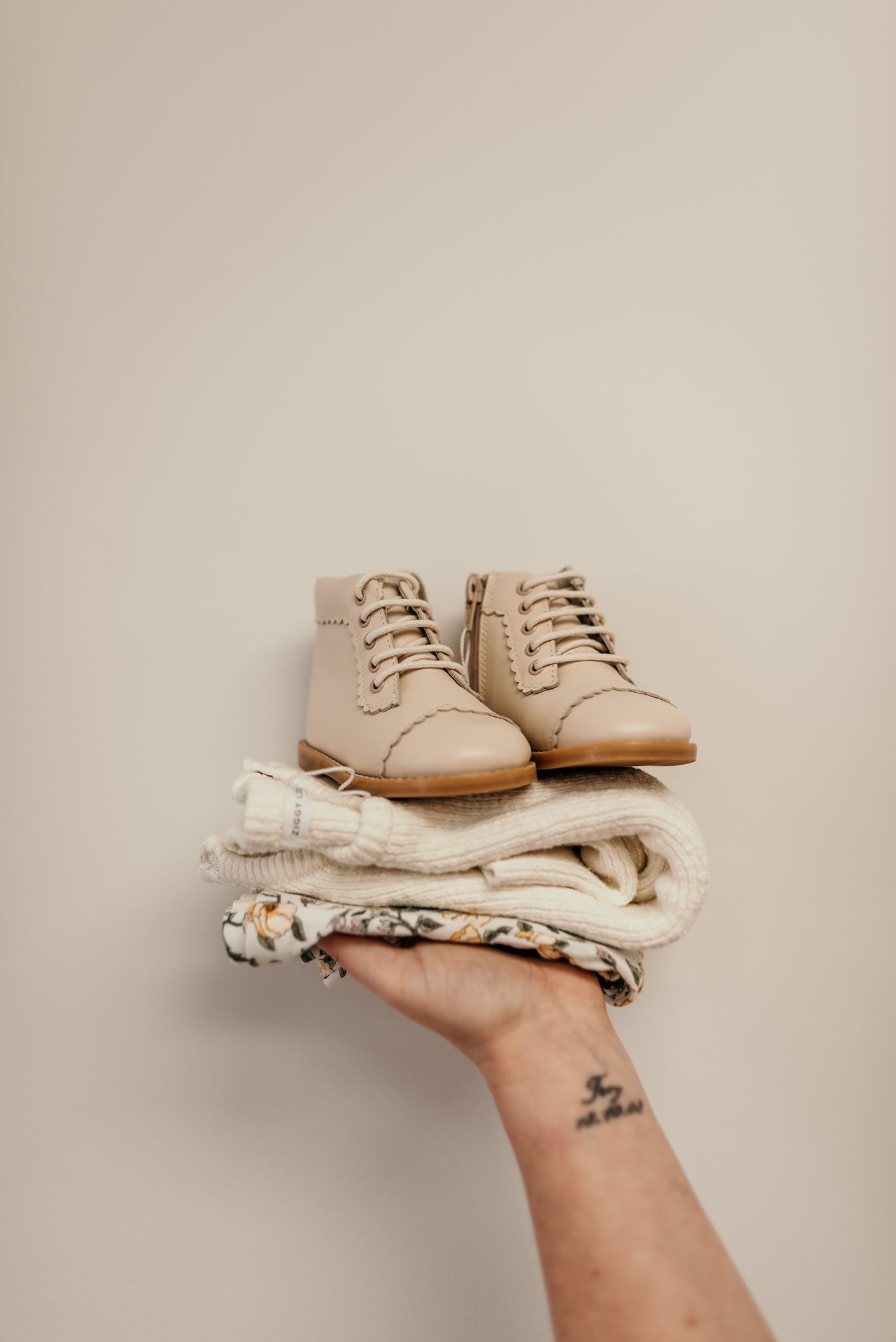 Beige leather boots stacked on folded neutral-colored clothing held by a tattooed hand in Christchurch shop.