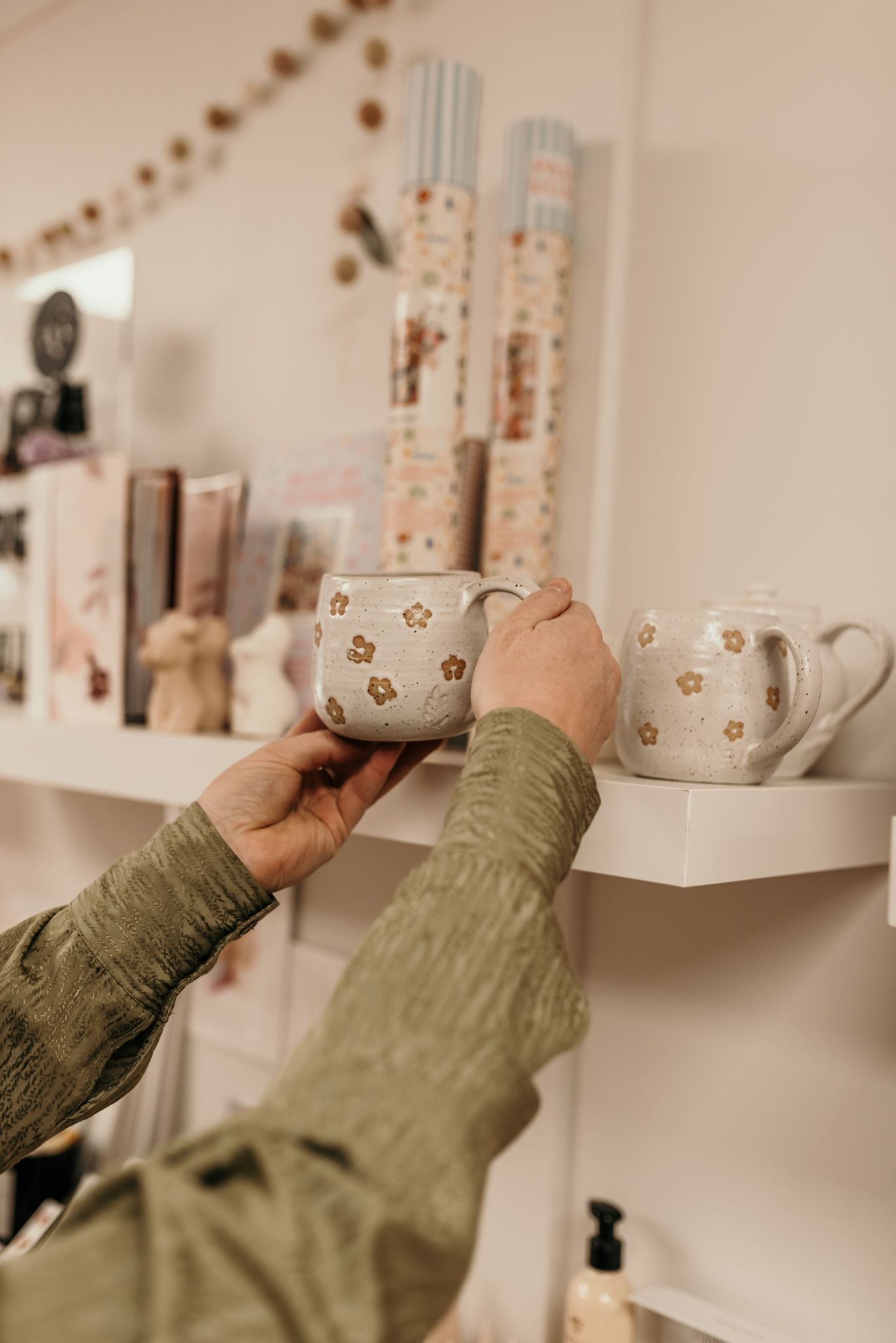 Hands reaching for decorative ceramic mugs with star patterns on white shelving in Christchurch shop.