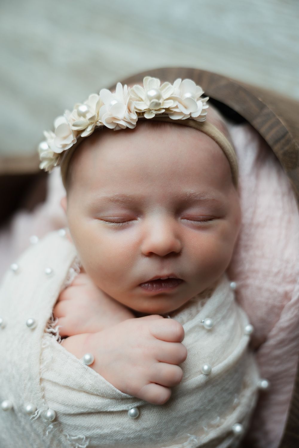 A baby wrapped in beige cloth with pearls and a bow is sleeping