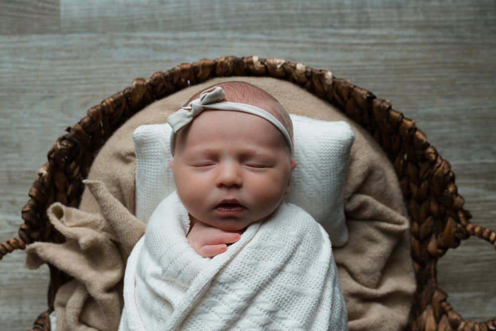 A baby wrapped in white cloth and a bow is sleeping in a basket