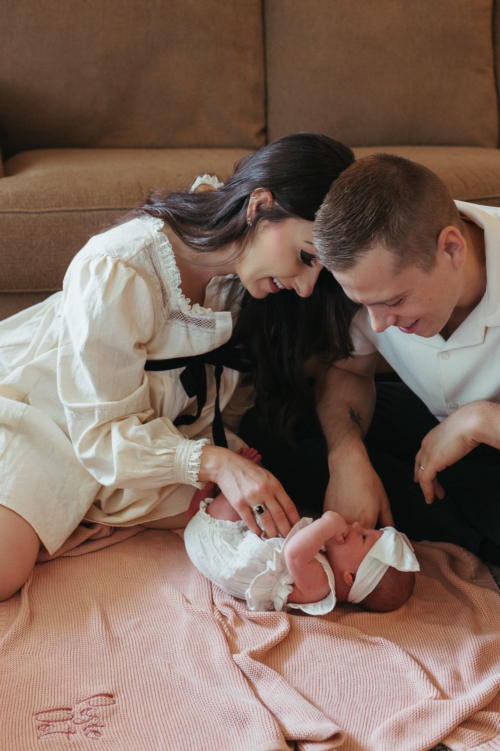 A man and woman are sitting on the ground playing with their small baby who is laying on a pink blanket