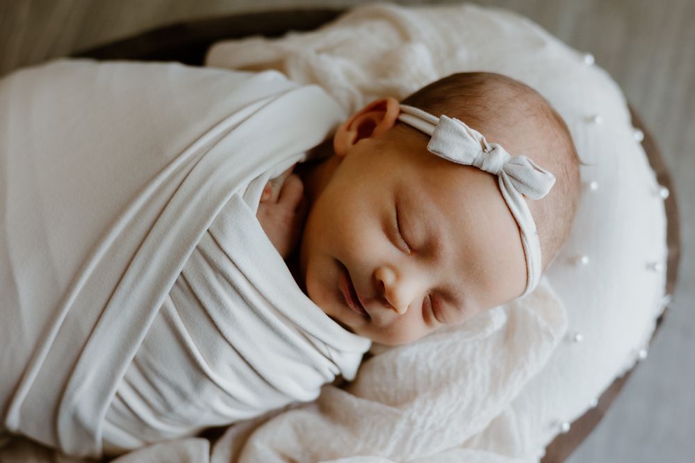 A baby wrapped in beige cloth and a bow is sleeping