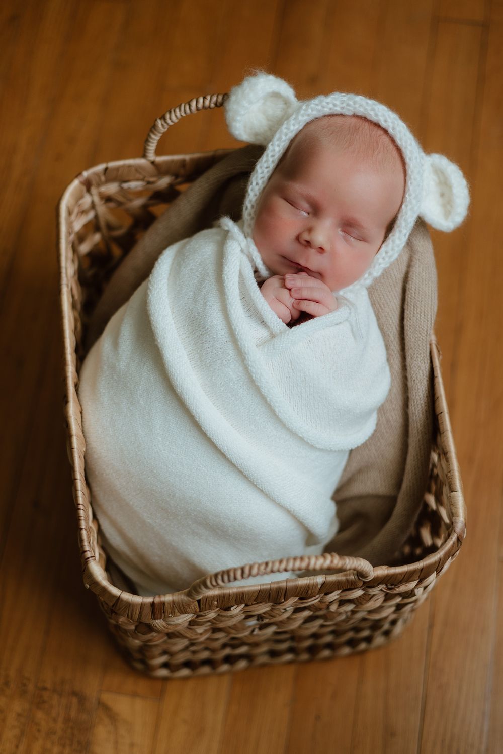 A baby wrapped in white cloth and a bonnet is sleeping in a basket