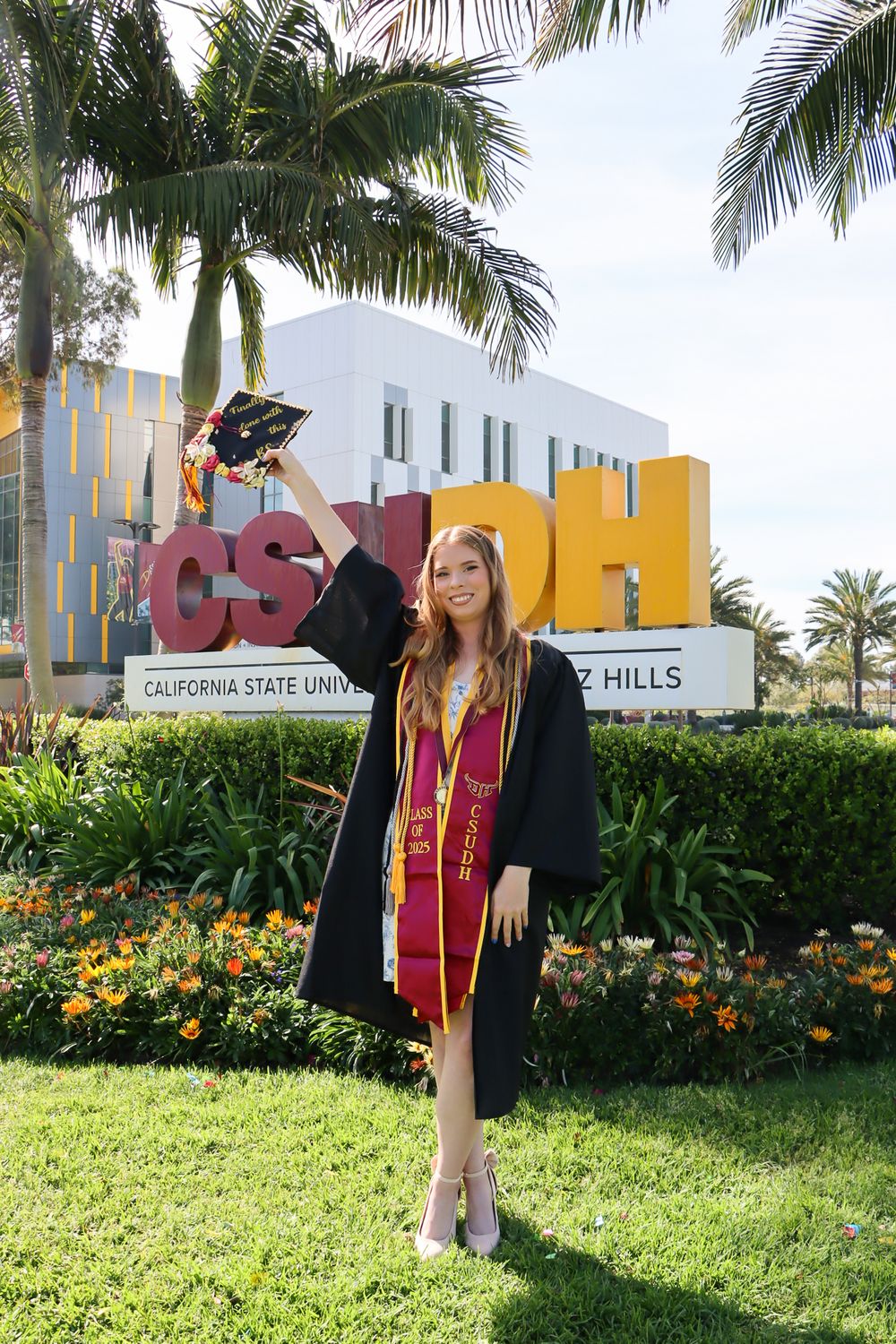Graduate celebrates in front of California State University signage with palm trees.