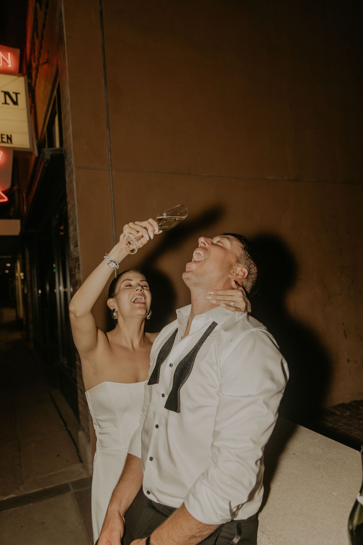A bride and groom laugh joyfully together during their wedding celebration in a dimly lit venue.