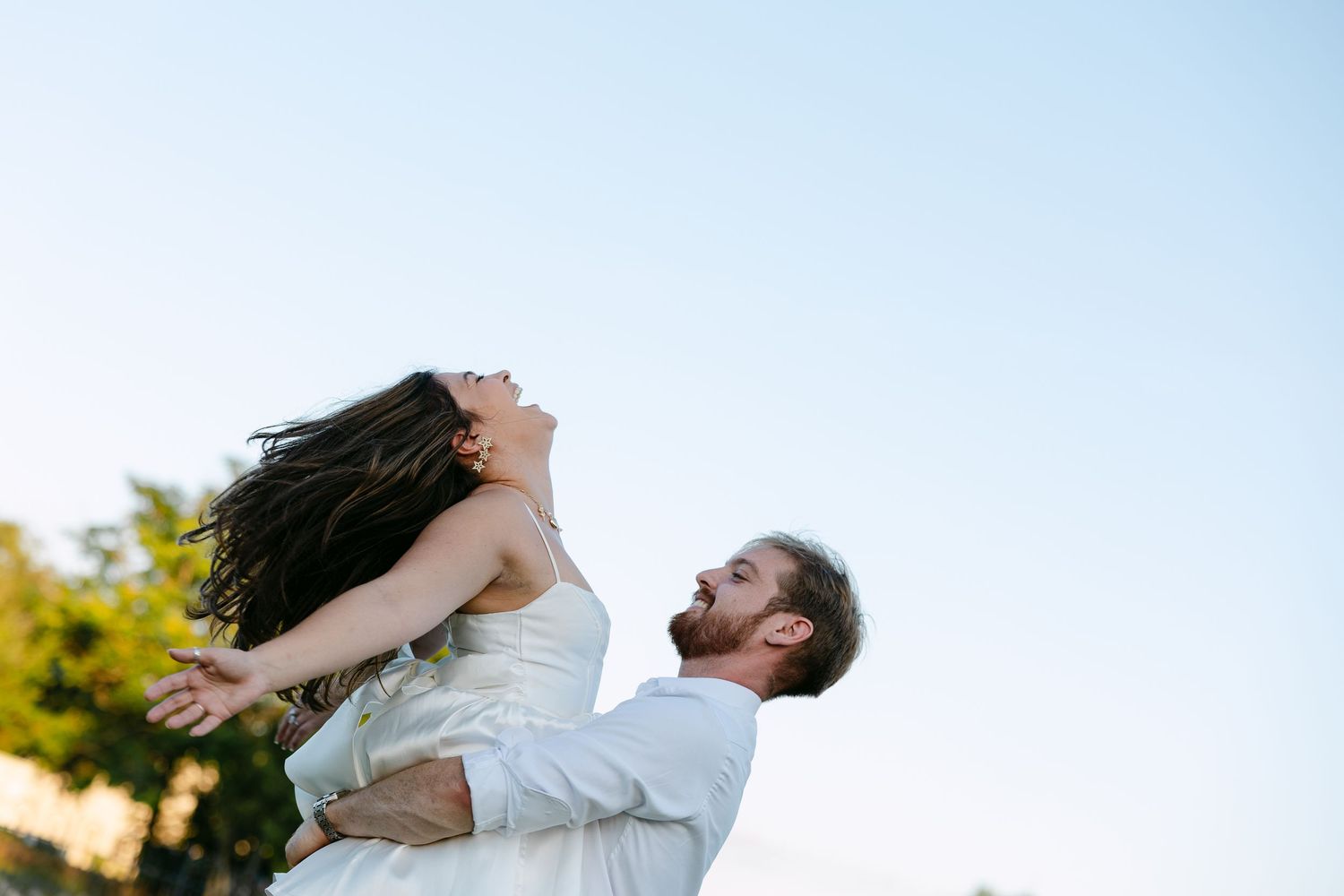 Couple in white dress and jeans wading in a serene creek surrounded by cypress trees with exposed roots.