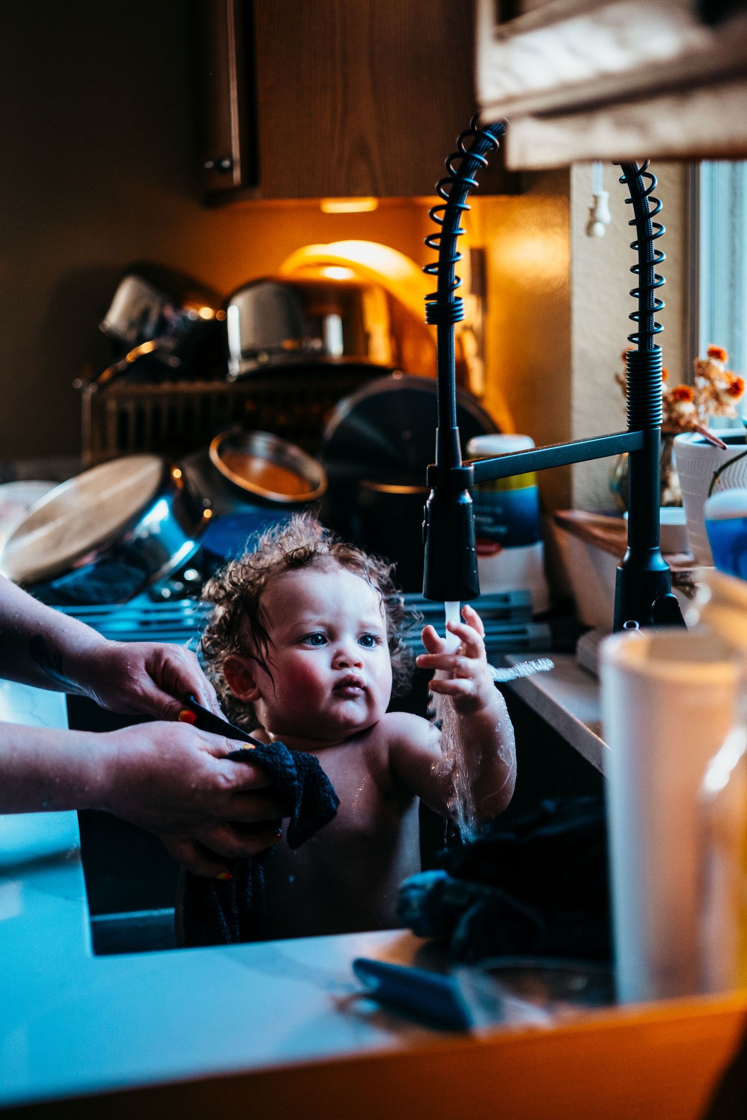Color image of one year old boy bathing in a kitchen sink and reaching for the water coming out of the faucet
