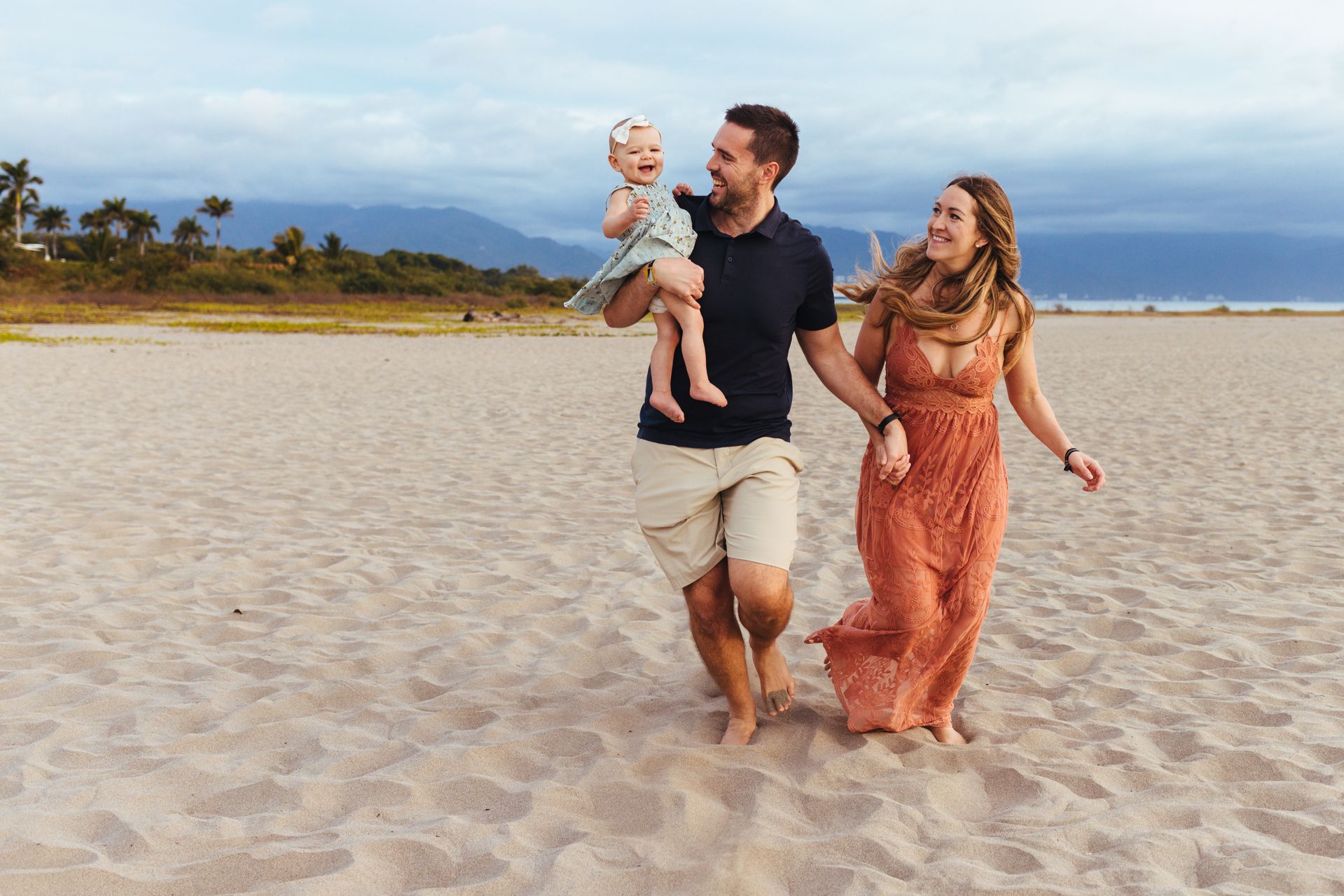 Family running together on sandy beach with mountains in background.