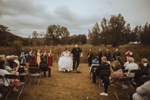 An outdoor wedding ceremony with guests seated on chairs in a rustic field setting.