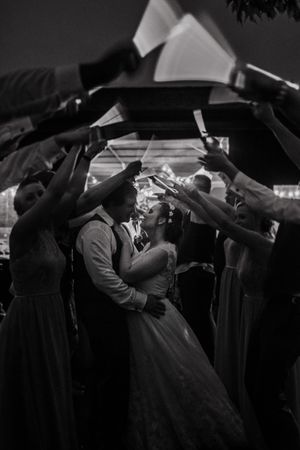Black and white photo of newlyweds kissing under archway formed by guests holding sparklers.