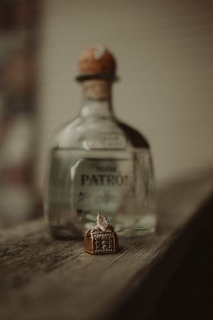 A bottle of Patron tequila sits next to a small decorative ring box on a wooden surface.
