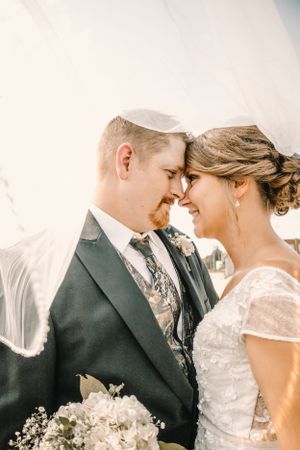 A tender wedding day moment captured under a flowing white veil with soft natural lighting.