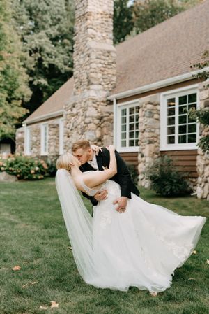 A romantic dip pose in front of a stone cottage with a flowing wedding dress.
