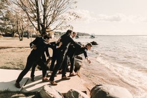 Wedding party having fun posing dramatically by waterfront rocks.